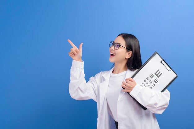 Una joven oftalmóloga con gafas sosteniendo un gráfico optométrico sobre azul, concepto de salud