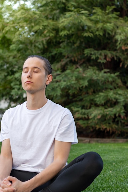 Joven con los ojos cerrados respirando profundamente el aire fresco y limpio rodeado de naturaleza en un parque