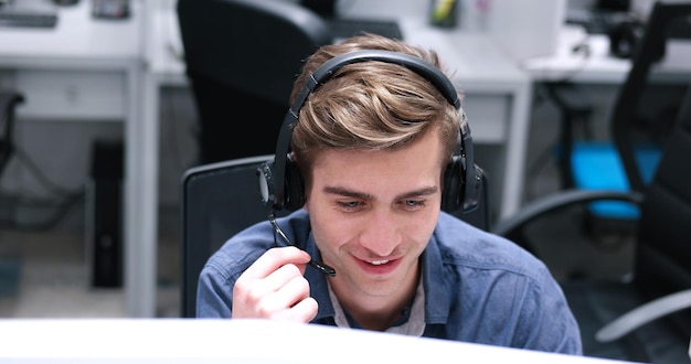 joven operador de centro de llamadas masculino sonriente haciendo su trabajo con un auricular