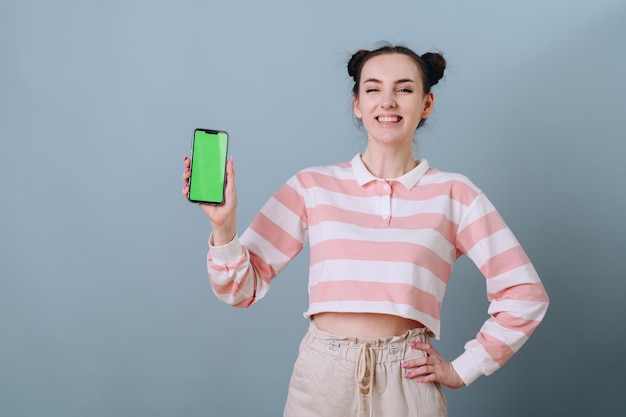 joven operadora gerente parada en una pared vacía con una expresión idiota y muestra un teléfono verde