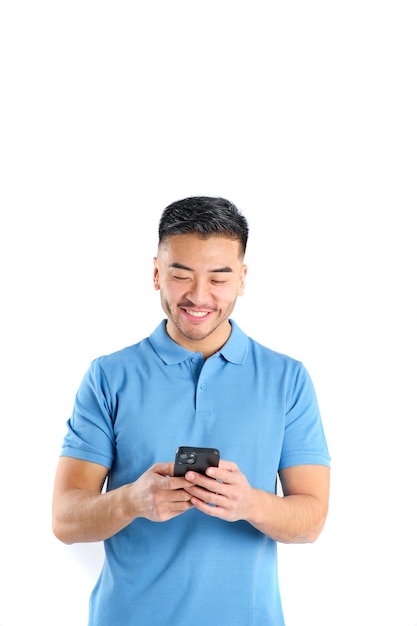 Foto un joven oriental sonriente con una camiseta de polo azul usando su teléfono inteligente sobre un fondo blanco