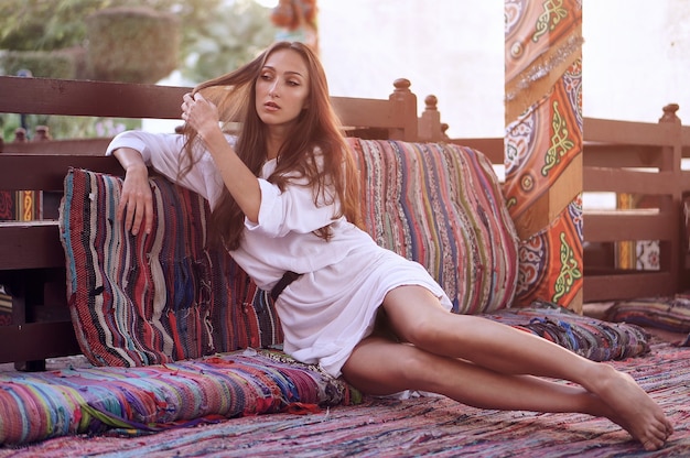 Joven oriental en vestido blanco relajante en el interior oriental tradicional en la ciudad árabe