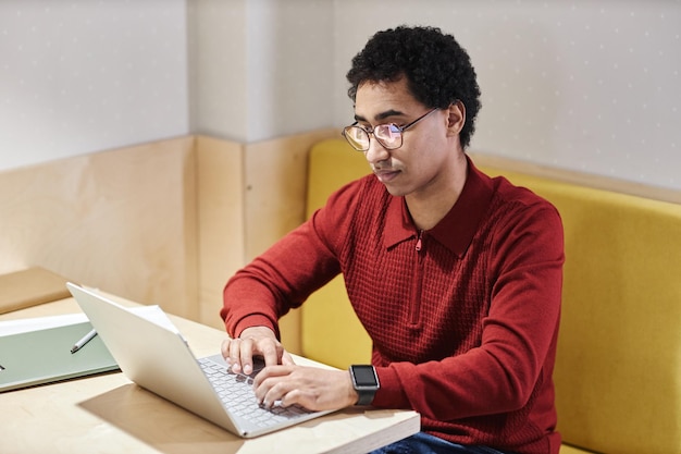 Un joven de Oriente Medio con gafas y usando una computadora.