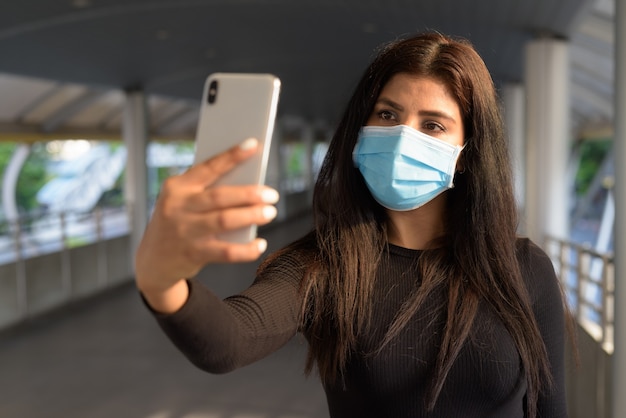 Joven de origen indio con máscara tomando selfie en la pasarela