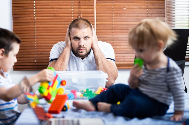 El joven padre se cubrió los oídos con fuertes gritos, interrupciones de los hijos de sus hijos mientras trabajaba en la casa