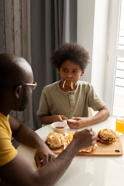 Foto joven padre e hijo comiendo hamburguesas y papas fritas juntos