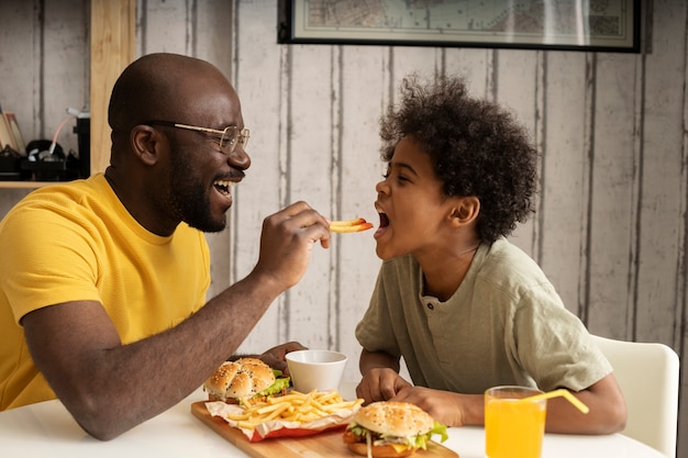 Foto joven padre e hijo comiendo hamburguesas y papas fritas juntos