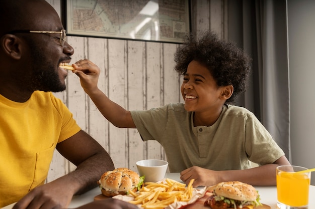 Joven padre e hijo comiendo hamburguesas y papas fritas juntos