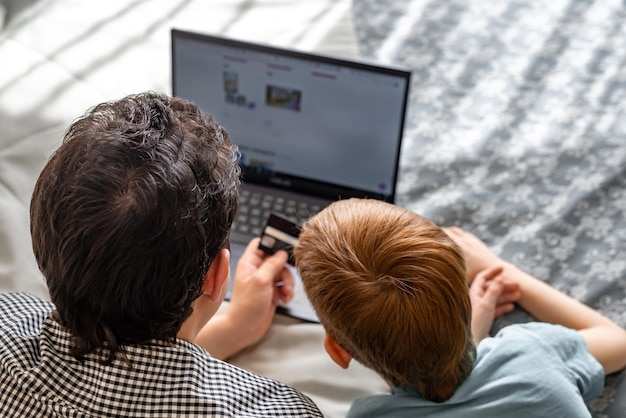 Joven padre e hijo comprando en línea juntos tiempo familiar Niño pelirrojo y papá en la computadora portátil eligen compras vista trasera