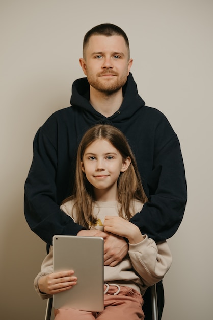 Un joven padre feliz con barba abraza a su linda hija usando tableta