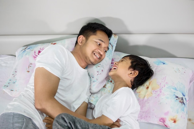 Un joven padre feliz haciendo cosquillas a su hijo en la cama.