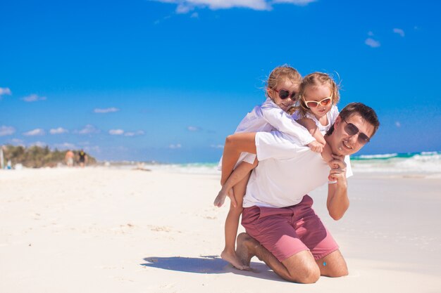 Joven padre feliz y pequeñas hijas que se divierten en la playa blanca en un día soleado