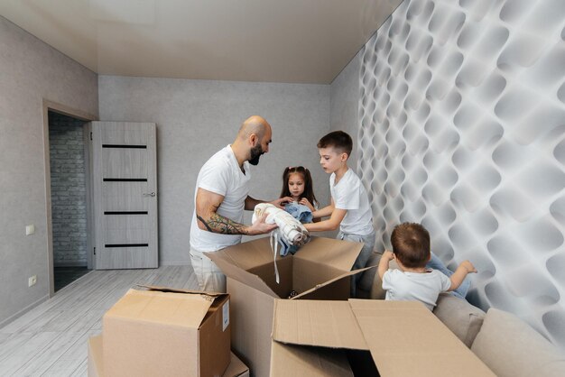 Un joven padre con hijos desempaca una caja de cosas después de mudarse a un nuevo apartamento Compra de bienes raíces Entrega de inauguración de la casa y transporte de bienes