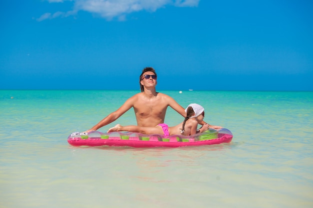 Joven padre con linda hija en un colchón de aire en el mar