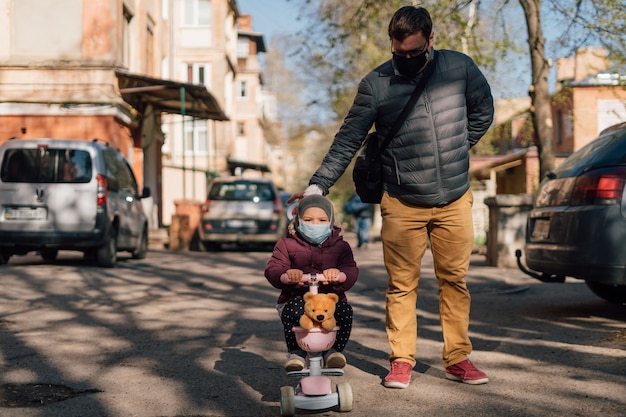 Joven padre con niño en scooter caminando afuera en máscaras médicas.