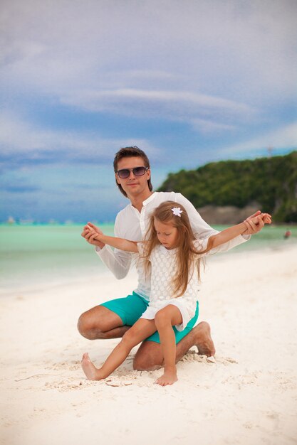 Foto joven padre y su pequeña hija sentada en la playa tropical de arena blanca