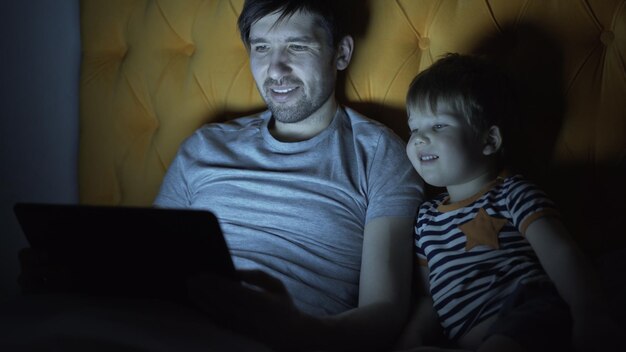 Joven padre y su pequeño hijo viendo una película de dibujos animados usando una computadora portátil