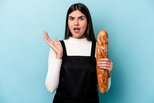 Foto joven panadero caucásico sosteniendo una hogaza de pan aislado de fondo azul sorprendido y conmocionado