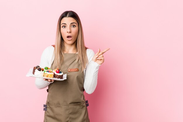 Joven panadero mujer sosteniendo dulces apuntando hacia el lado