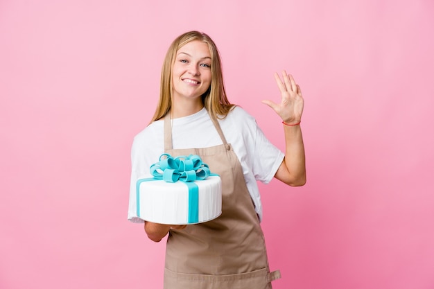 Joven panadero ruso sosteniendo un delicioso pastel sonriendo alegre mostrando el número cinco con los dedos.