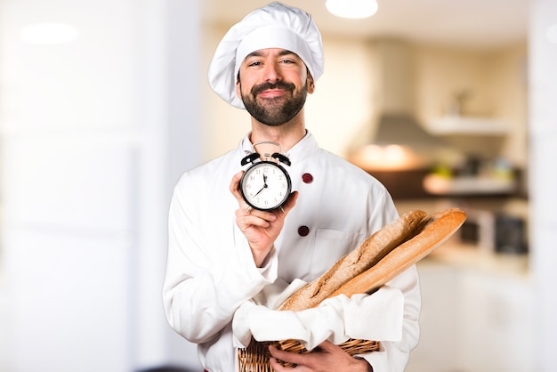 Joven panadero sosteniendo un poco de pan y la celebración de reloj de época en la cocina