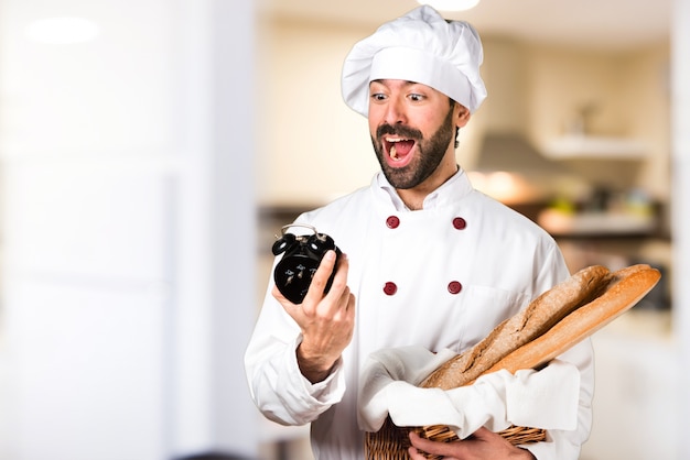 Joven panadero sosteniendo un poco de pan y la celebración de reloj de época en la cocina