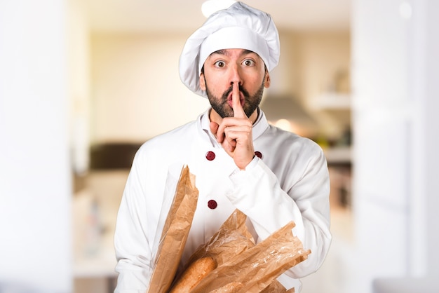 Joven panadero sosteniendo un poco de pan y hacer silencio gesto en la cocina