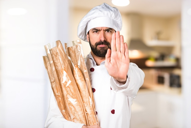 Joven panadero sosteniendo un poco de pan y haciendo señal de stop en la cocina