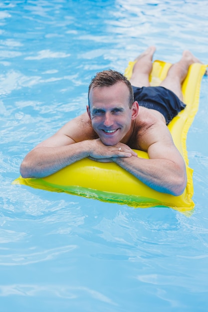 Un joven en pantalones cortos disfruta del parque acuático flotando en un gran anillo inflable en una piscina azul brillante sonriendo a la cámara Vacaciones de verano