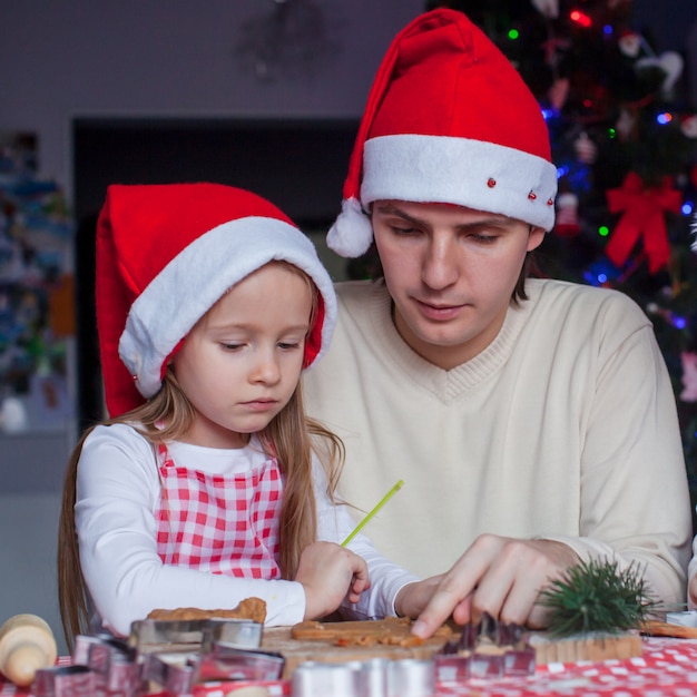 Joven papá con hija pequeña en Santa hat hornear galletas de jengibre de Navidad