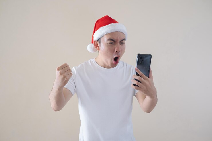 El joven Papá Noel asiático está emocionado mientras mira el teléfono inteligente