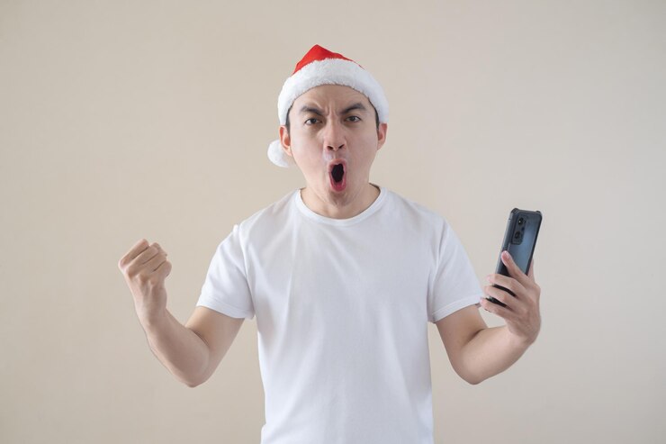 El joven Papá Noel asiático está emocionado mientras sostiene el teléfono inteligente y mira la cámara