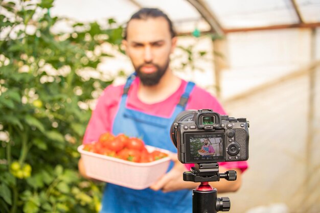 Joven parado frente a la cámara y sosteniendo una canasta de tomate