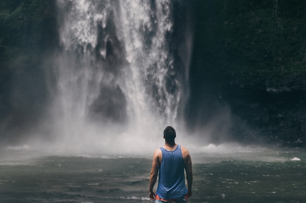 Joven parado frente a la poderosa cascada Nungnung en Bali