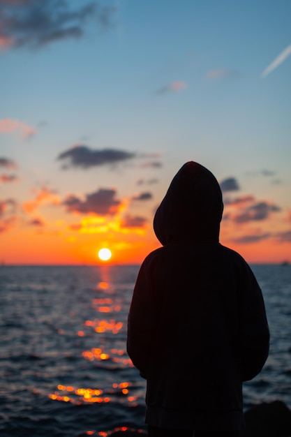 Joven parado en la playa mirando la puesta de sol