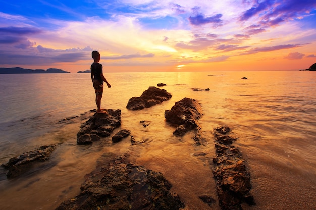 joven parado en roca en el mar con puesta de sol cielo, playa Tarn-khu en Trat, Tailandia