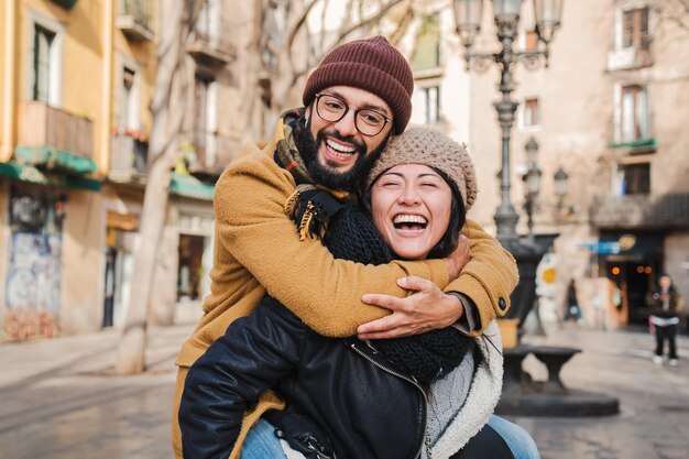 Joven pareja afectuosa multirracial riendo y sonriendo juntos dando un paseo a espaldas divirtiéndose abrazándose y abrazándose en una cita romántica dos amigos unidos al aire libre foto de alta calidad