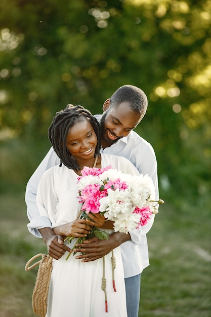 Joven pareja africana en abrazo romántico en un campo. Amantes jóvenes en un campo con flores.