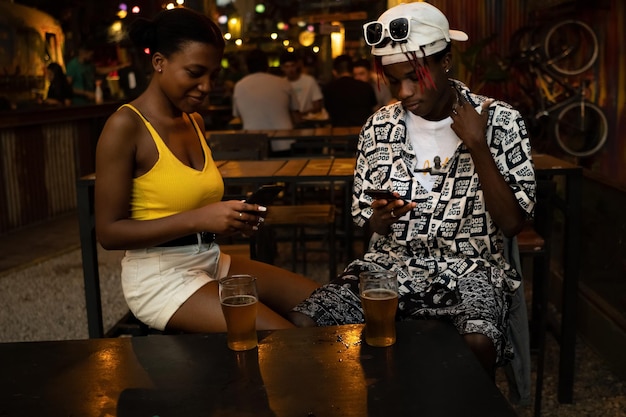 Joven pareja afro ignorando el uno al otro en un bar mientras usa teléfonos móviles.