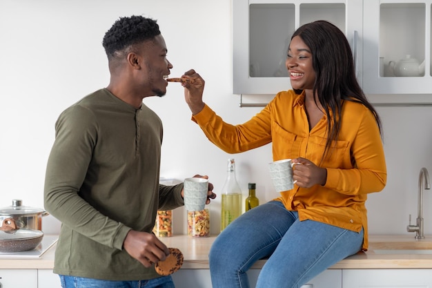 Joven pareja afroamericana divirtiéndose mientras come bocadillos en la cocina