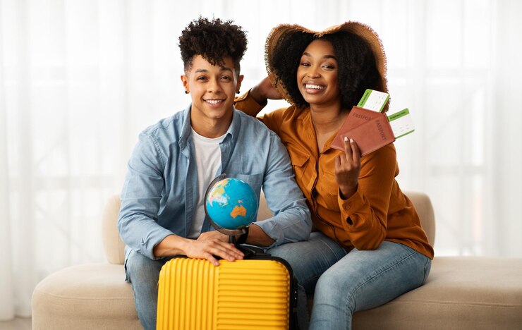 Una joven pareja afroamericana sonriente con sombrero y maleta muestra pasaporte y boletos