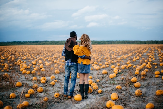 Una joven pareja de agricultores de pie en un campo de calabazas