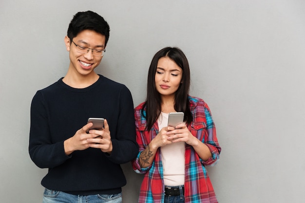 Joven pareja amorosa asiática utilizando teléfonos móviles.