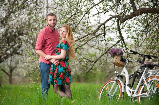 Joven pareja amorosa con bicicletas en el jardín de primavera