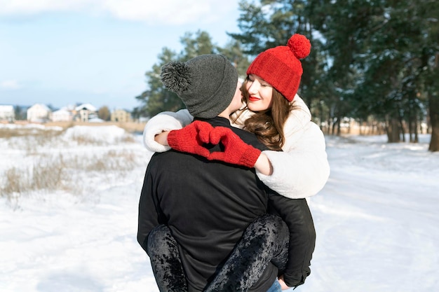 Joven pareja amorosa en el bosque de invierno Feliz joven mantiene las manos en forma de corazón y abraza a su novio Día soleado