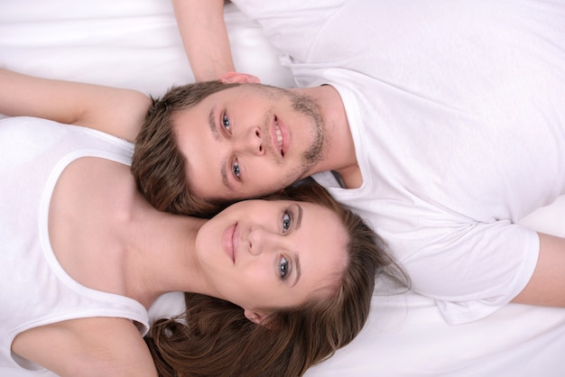 Joven pareja amorosa en una cama blanca.