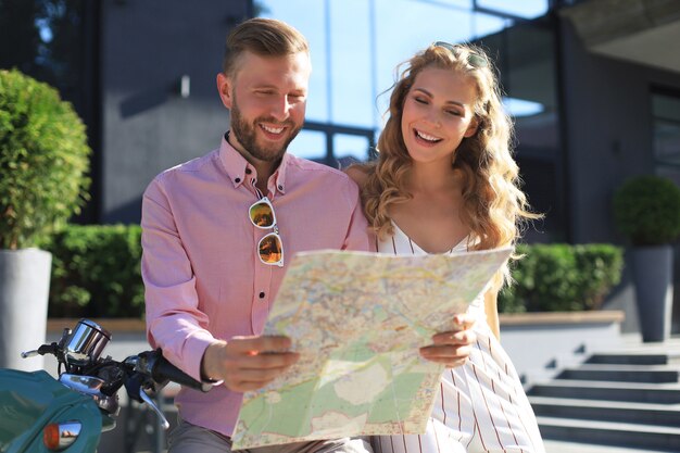 Joven pareja amorosa feliz mirando el mapa y sentado en scooter.