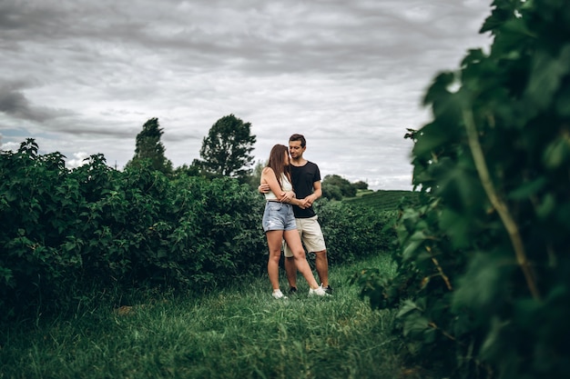 Foto joven pareja amorosa, mujer y hombre, abrazando suavemente con los ojos cerrados en el campo de grosella verde. primer plano con hojas borrosas