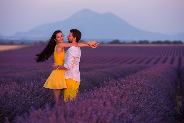 joven pareja amorosa pasando un momento romántico abrazándose y besándose en el campo de flores de lavanda púrpura al atardecer