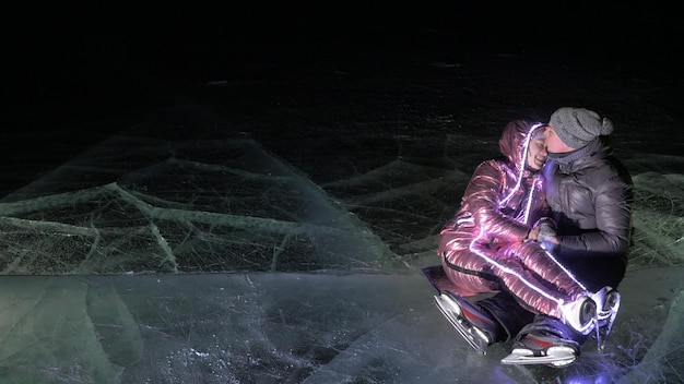 Joven pareja amorosa patinando en la pista de hielo por la noche El hombre y la mujer se besan abrazo divertirse aprender a patinar Hacer el amor sobre hielo Hielo iluminado a contraluz debajo